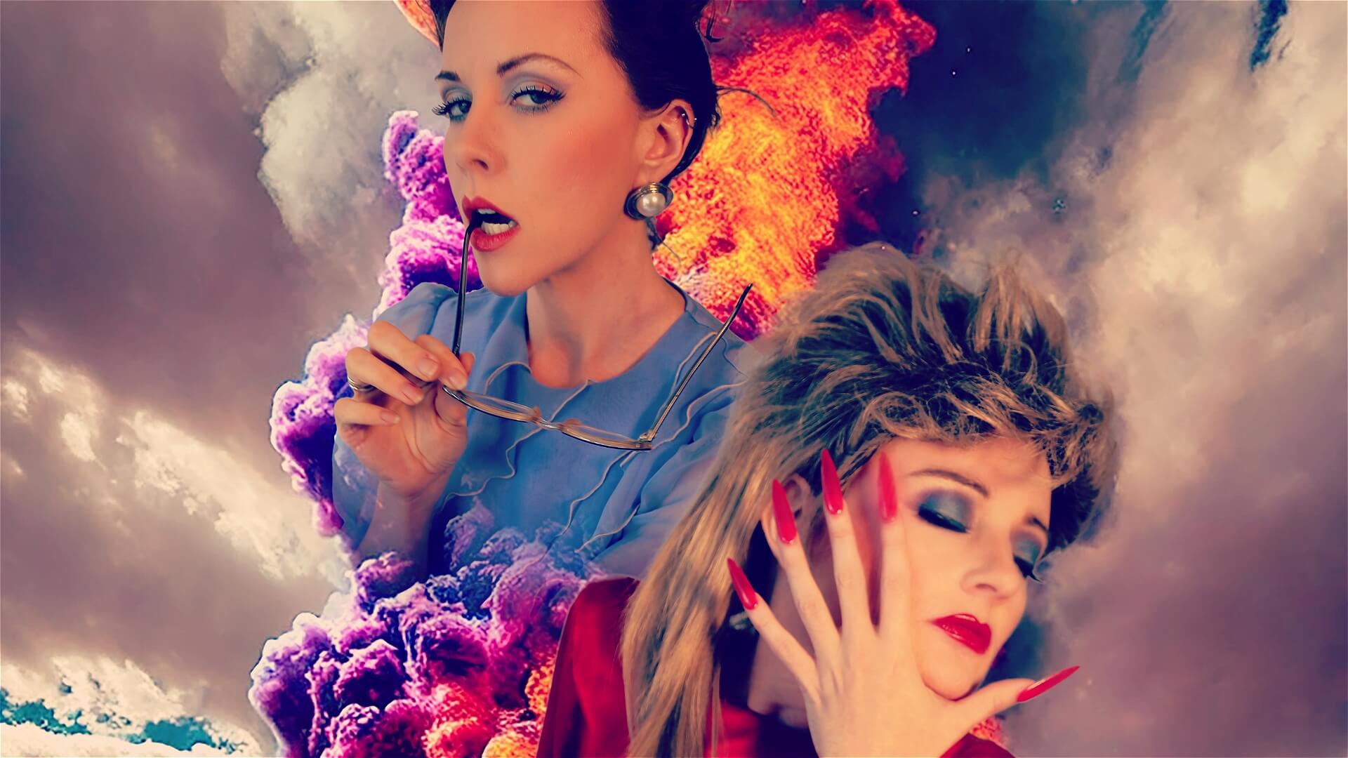 Two women pose against a dramatic, colorful background of swirling clouds and fire. One wears vintage-style glasses and earrings, while the other has bold makeup, red nails, and a feathered hairstyle, with her eyes closed and hand on her face.