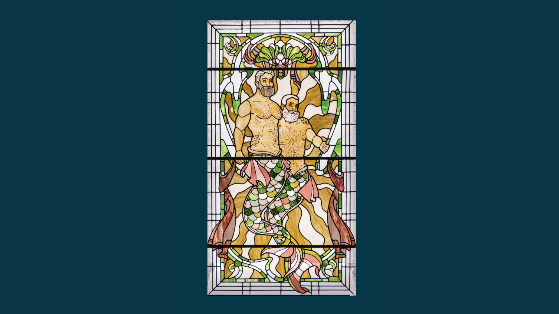 Stained glass window depicting two bearded mermen, entwined, with green and pink tails, surrounded by seaweed and seashell designs on a dark blue background.
