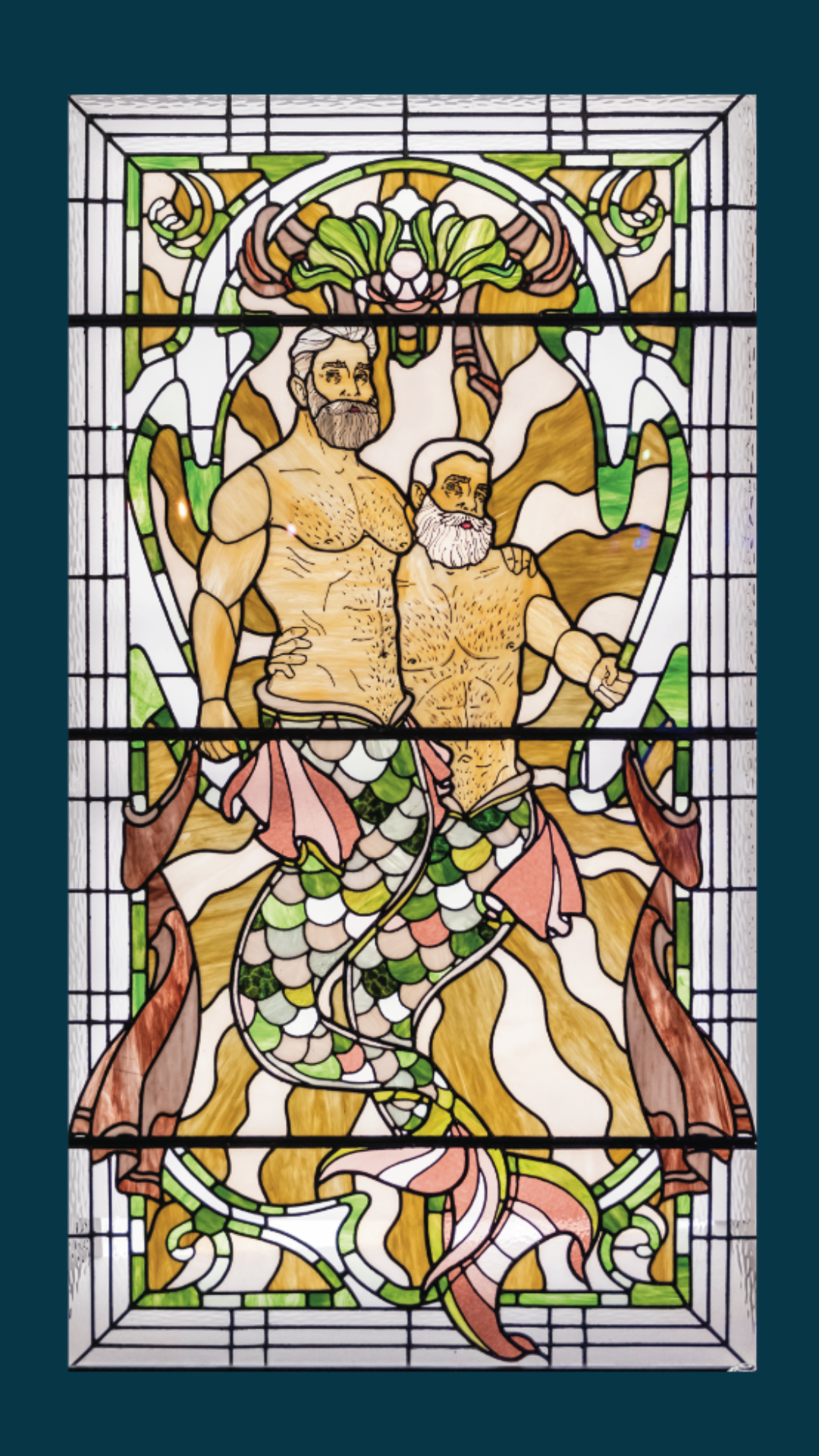 Stained glass window showing two bearded mermen with colorful fish tails, standing close together with an arm around each other, surrounded by decorative patterns and seaweed designs.