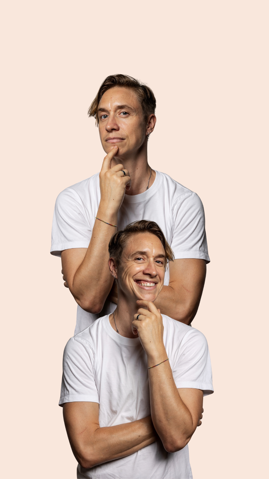 Two men wearing white t-shirts pose together with their hands on their chins, one looking thoughtful and the other smiling, against a plain light background.
