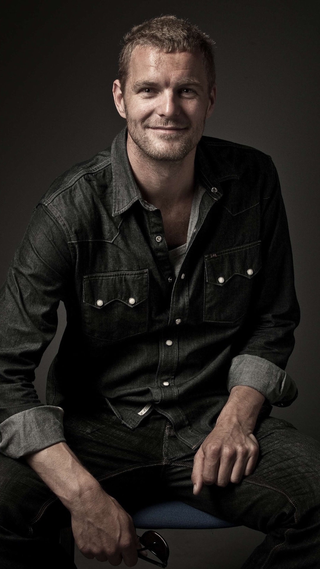 A smiling man wearing a dark denim button-down shirt.
