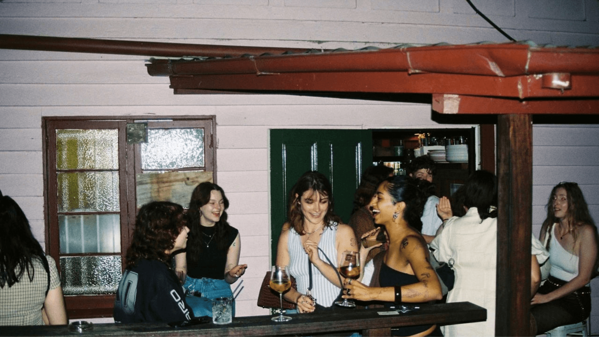A group of young adults socializing and drinking at an outdoor bar counter at night.