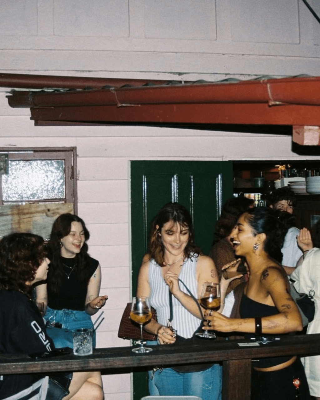 Four young women laughing and talking while holding drinks at a bar.